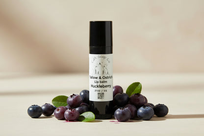 Lip balm with a black cap and white label on a white background and huckleberry accents