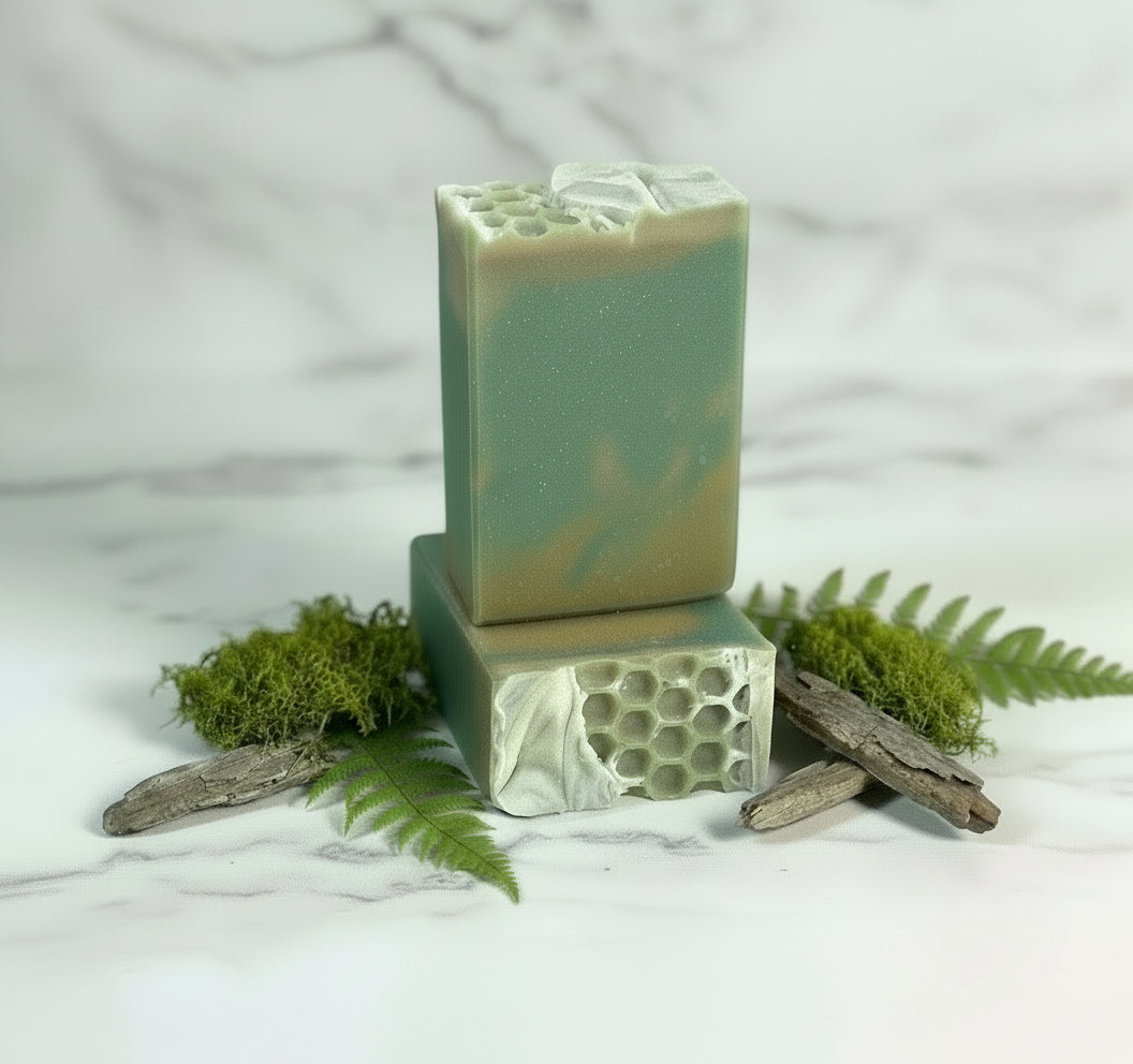 Two green soap bars with natural textures on a wooden surface with greenery.
