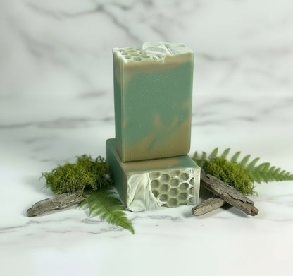 Two green soap bars with natural textures on a wooden surface with greenery.