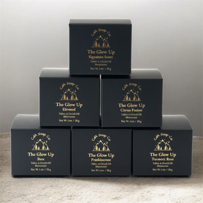 Stack of black face moisturizer boxes with 'The Glow Up' branding on a gray background