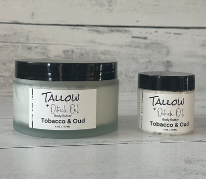 Two jars of Tallow + Ostrich Oil body butter on a wooden surface with a gray background.