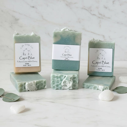 Three bars of Capri Blue soap on a wooden surface with a white background