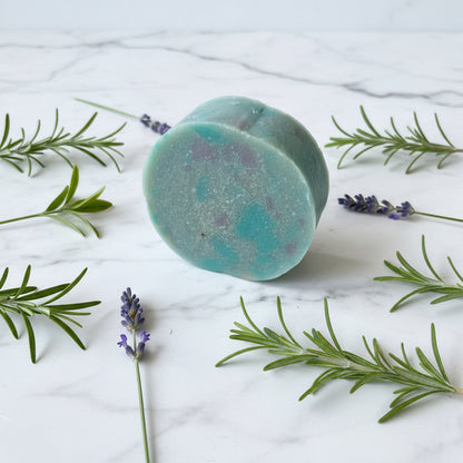Blue-green bath bomb with lavender and rosemary on a marble surface