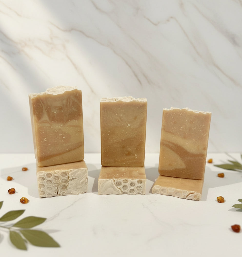 Five bars of natural soap with a marbled pattern on a white surface with a blurred plant background.