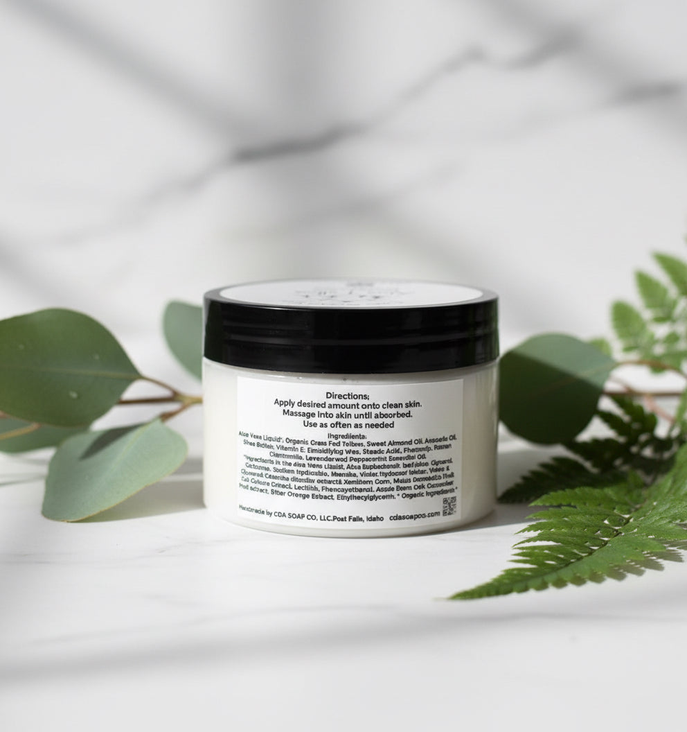 Jar of cream with a black lid on a white surface with green leaves in the background