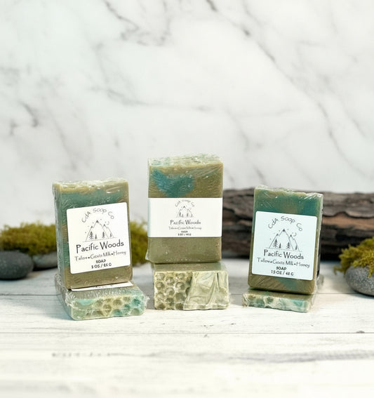 Three bars of soap labeled 'Pacific Woods' on a wooden surface with a natural background.