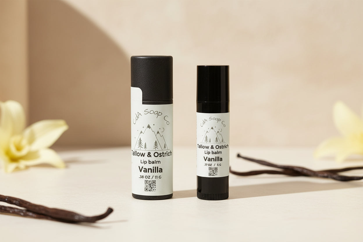 Two Black Tallow and Ostrich lip balm containers from CdA Soap Co. on a light background and vanilla bean accents. Vanilla scented/ flavored