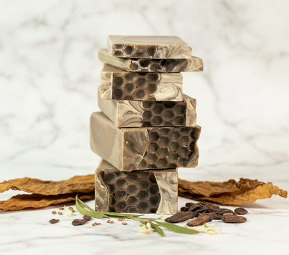 Stack of honeycomb-patterned soap bars with dried herbs and seeds on a white background
