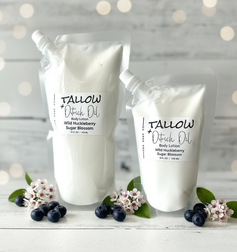 Two white body lotions with black text on a wooden surface with huckleberries and flowers.