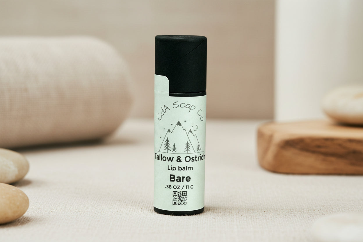 One black Kraft board lip balm container with white label featuring Mountain graphics on a white background. Label reads CdA Soap Co. Tallow & Ostrich Lip Balm. Bare. ( unscented/ unflavored ) 11 g weight