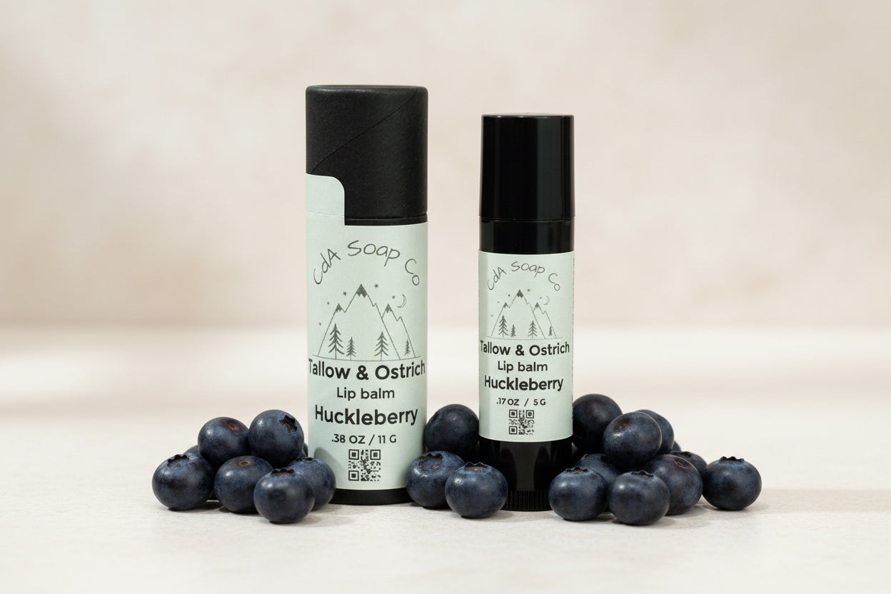 Two lip balm containers with labels on a light background and huckleberry accents
