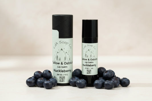 Two lip balm containers with labels on a light background and huckleberry accents