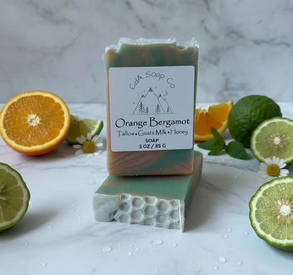 Bar of soap with 'CDA Soap Co' label surrounded by citrus fruits and herbs on a marble surface