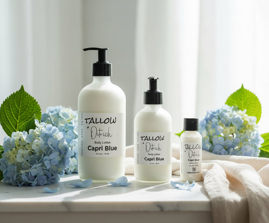 Three bottles of capri blue Tallow & ostrich oil CdA soap Co. body lotion on a marble surface with flowers and leaves.