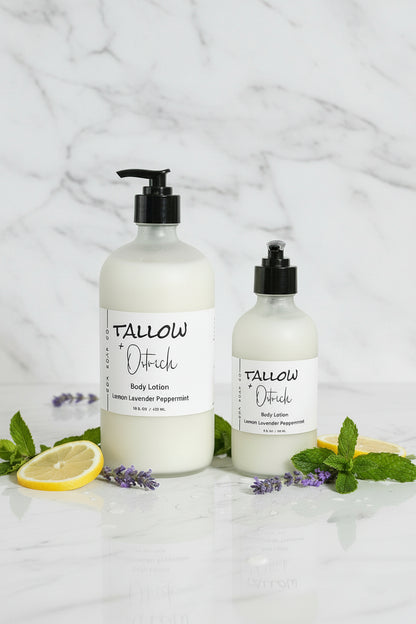 Two bottles of Tallow & Oatflesh body lotion on a white surface with lemons and mint leaves.