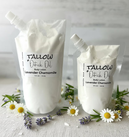 Two containers of Tallow + Oatrich Oil body lotion with lavender and chamomile flowers on a light background.