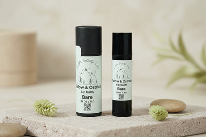 Two lip balm containers with black caps and white labels featuring Mountain graphics on a white background. Label reads CdA Soap Co. Tallow & Ostrich Lip Balm. Bare. For unscented/ unflavored stone and greenery accents 