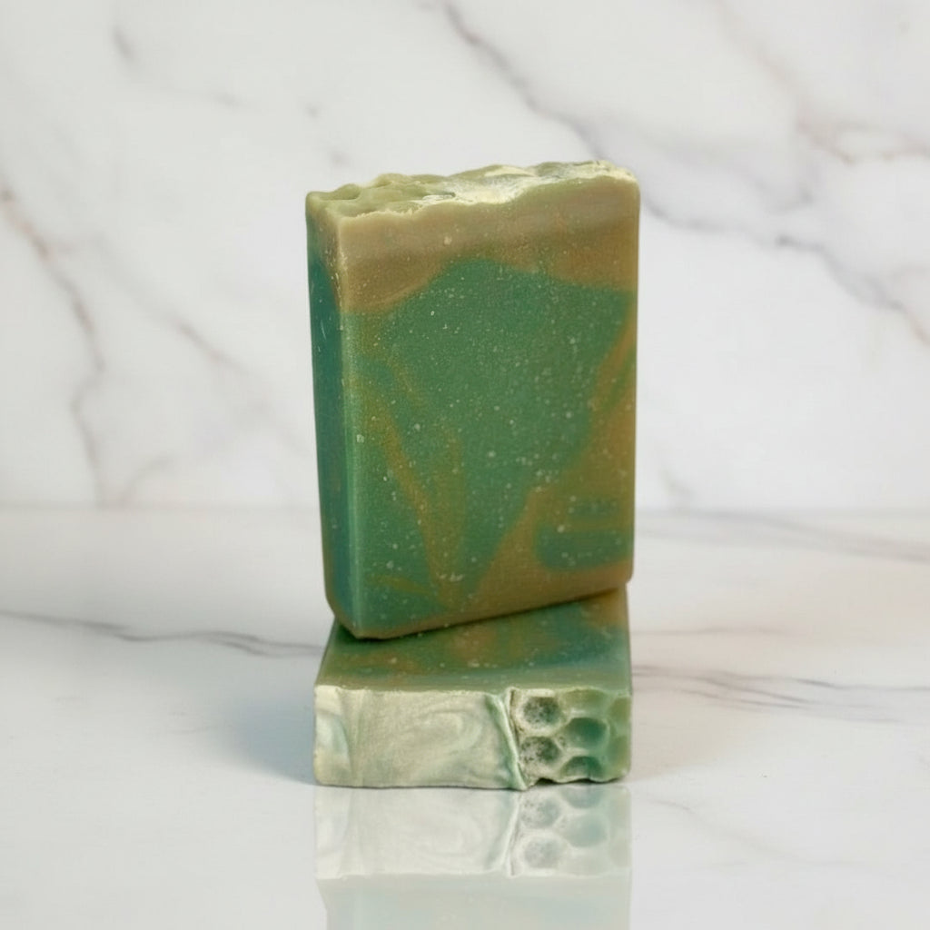 Two green soap bars on a wooden surface with a marble background