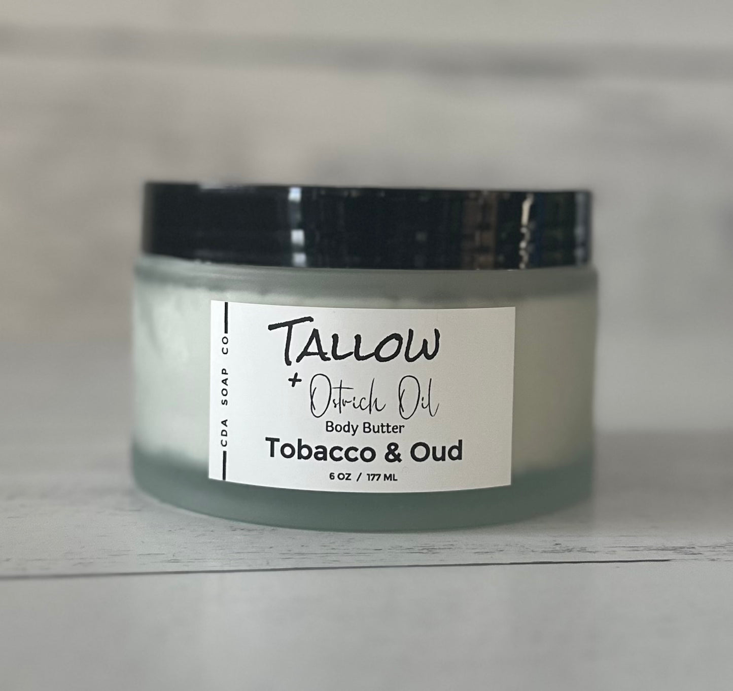 Jar of Tallow + Ostrich Oil body butter labeled 'Tobacco & Oud' on a neutral background