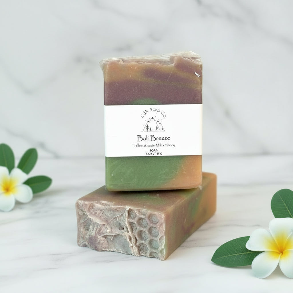 Two stacked soap bars with a visible brand label on a light blue fabric background with flowers and leaves.