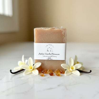 Bar of soap with 'Amber Vanilla Blossom' label surrounded by vanilla flowers and pods on a light surface.