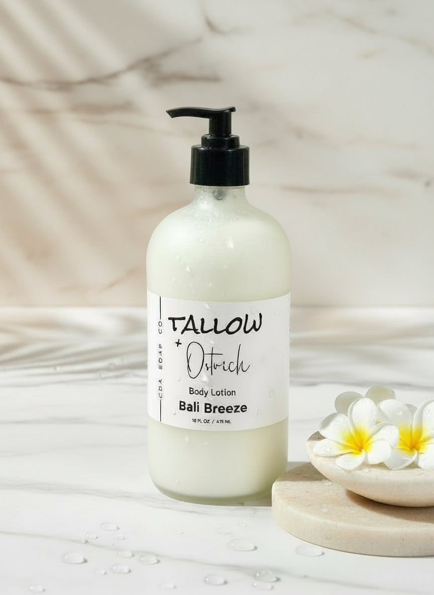 Bottle of Tallow + Oatrich Bali Breeze body lotion on a blurred background with flowers and towels.
