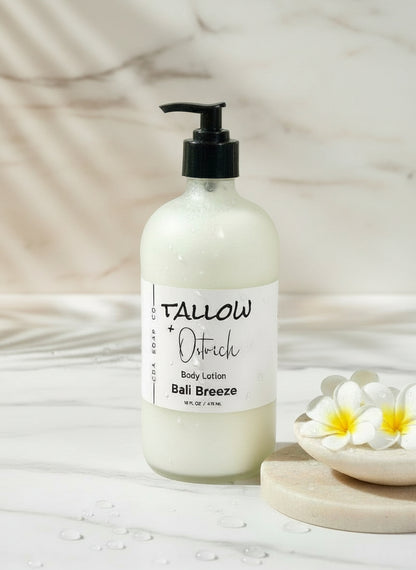 Bottle of Tallow + Oatrich Bali Breeze body lotion on a blurred background with flowers and towels.