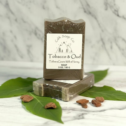 Bar of soap with a label on a wooden surface with leaves and soap pieces around