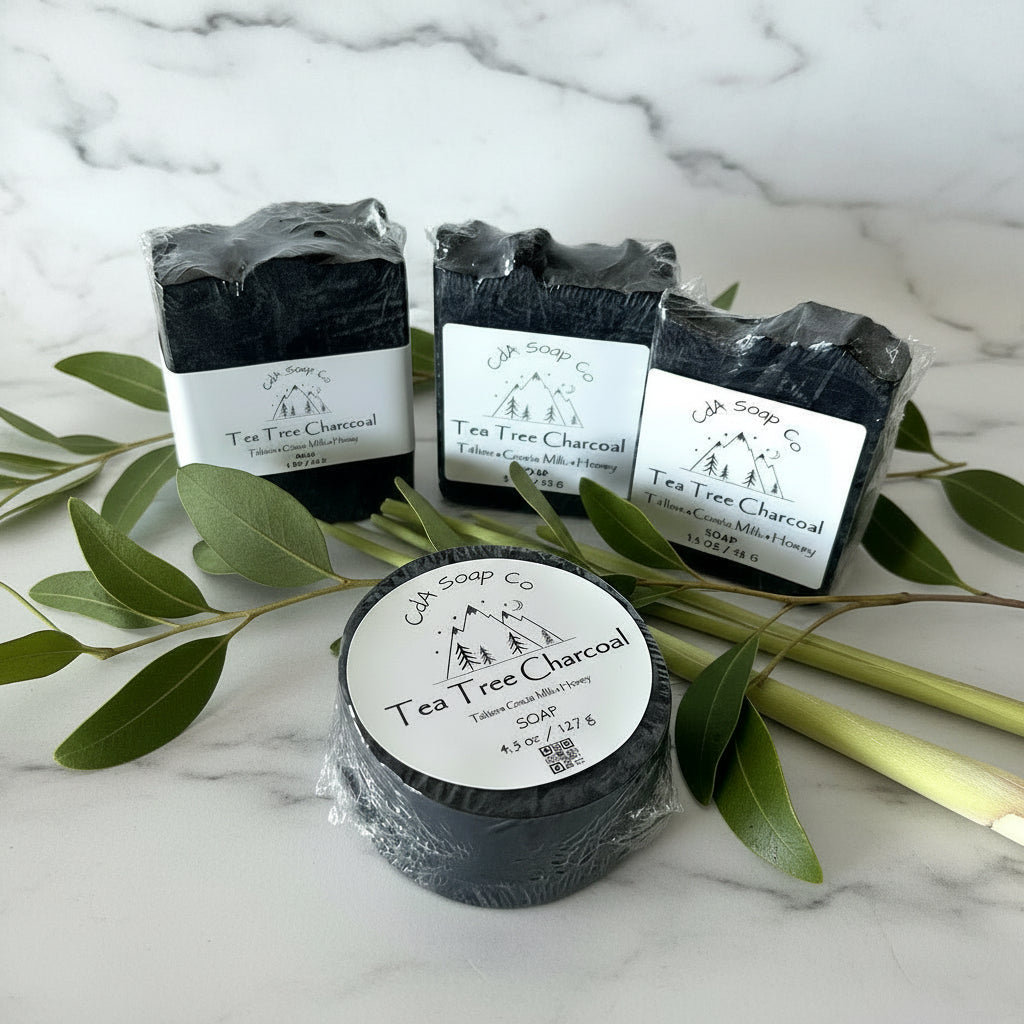 Tea Tree Charcoal soap bars with packaging on a white surface with green leaves.