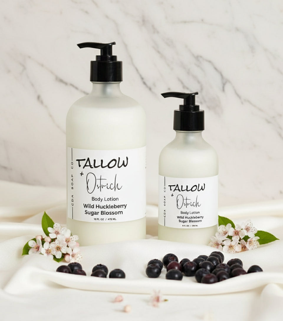Two bottles of Tallow & Ostrich body lotion on a light surface with huckleberry and flower accents