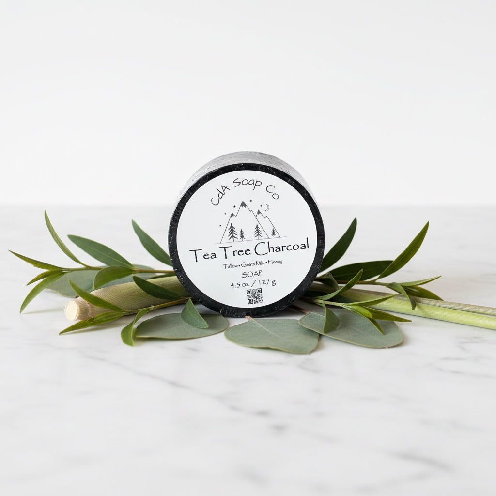 Jar of Tea Tree Charcoal soap from CdA Soap Co on a white background with green leaves.