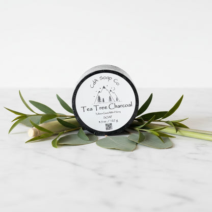 Jar of Tea Tree Charcoal soap from CdA Soap Co on a white background with green leaves.