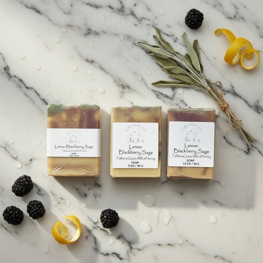 Three bars of soap labeled 'Lemon Blackberry Sage' on a textured surface with blackberries and sage leaves.