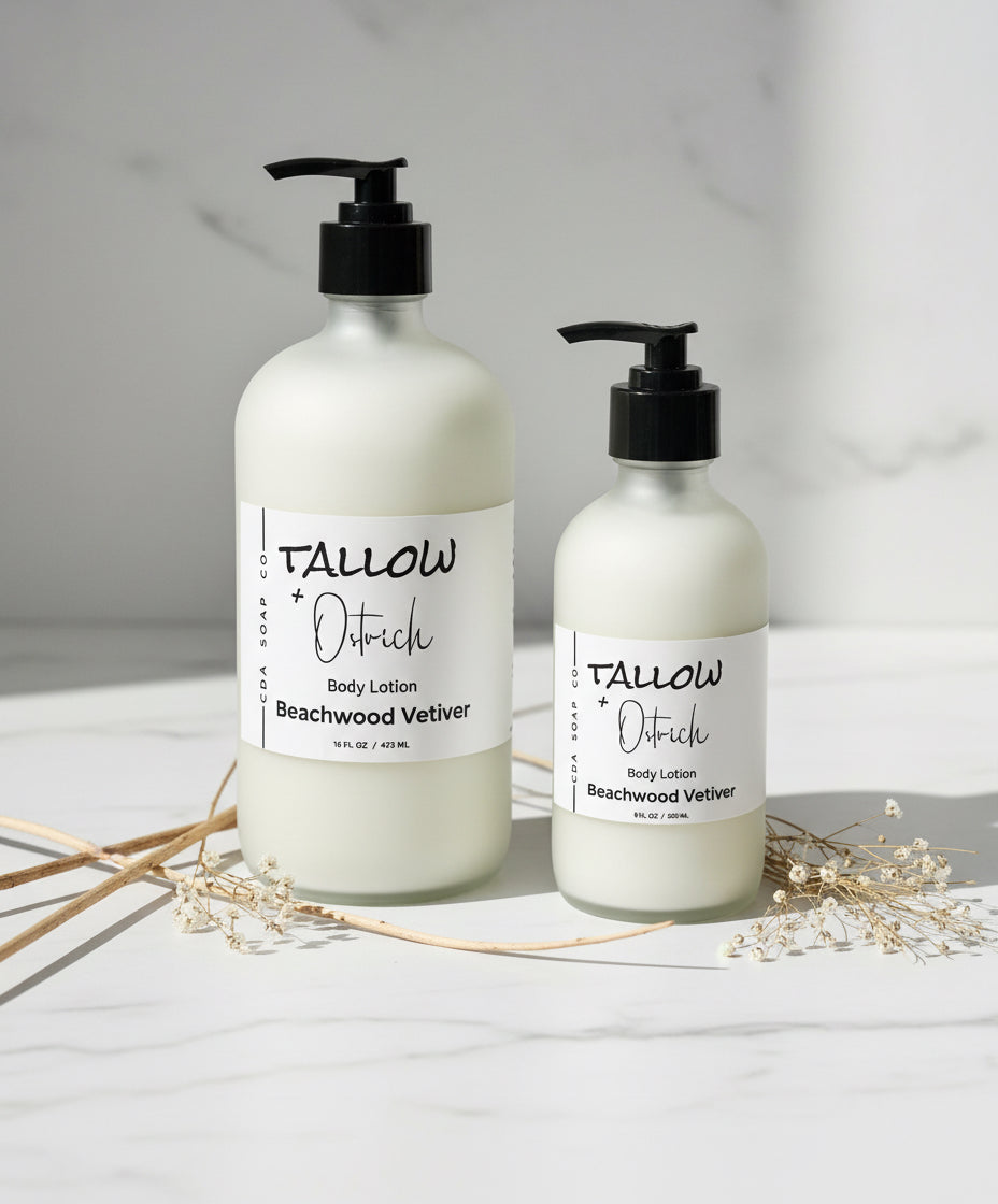 Two bottles of Tallow & Ostrich body lotion on a light surface with dried plants.