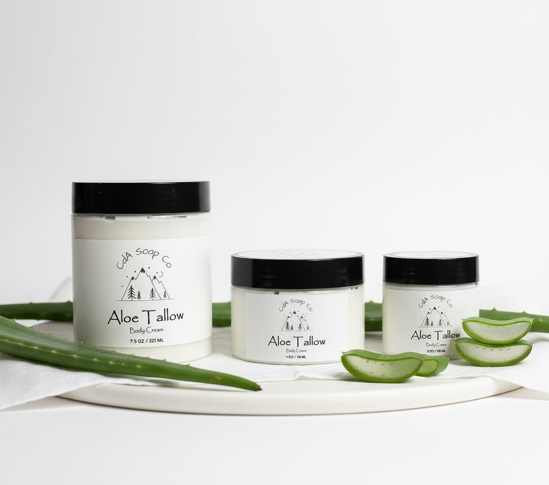 Three jars of Aloe Tallow body cream on a white background with aloe vera leaves.