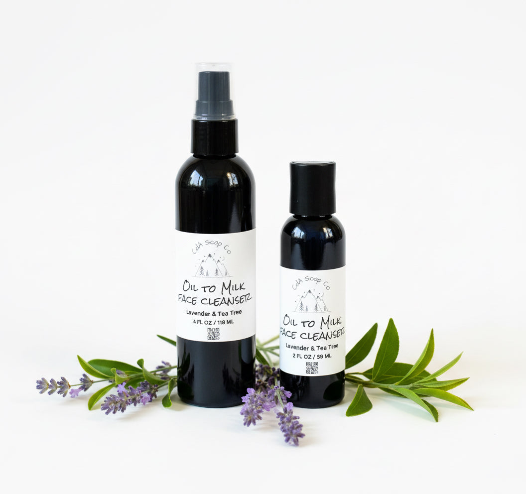 Two bottles of 'Oil to Milk Face Cleanser' with lavender and tea tree leaves on a white background