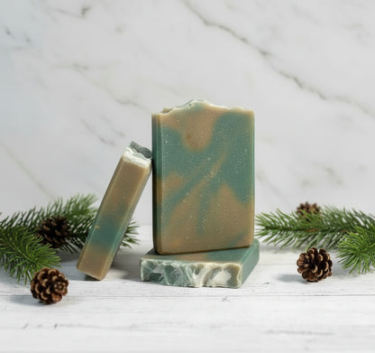 Bar of soap with green and brown swirled pattern on a wooden surface with a forest background