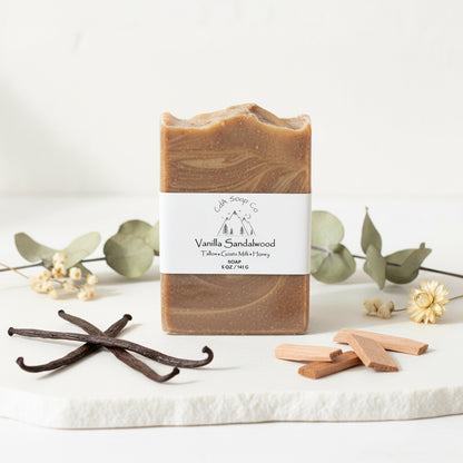 Vanilla sandalwood soap bar with vanilla beans and eucalyptus leaves on a white background