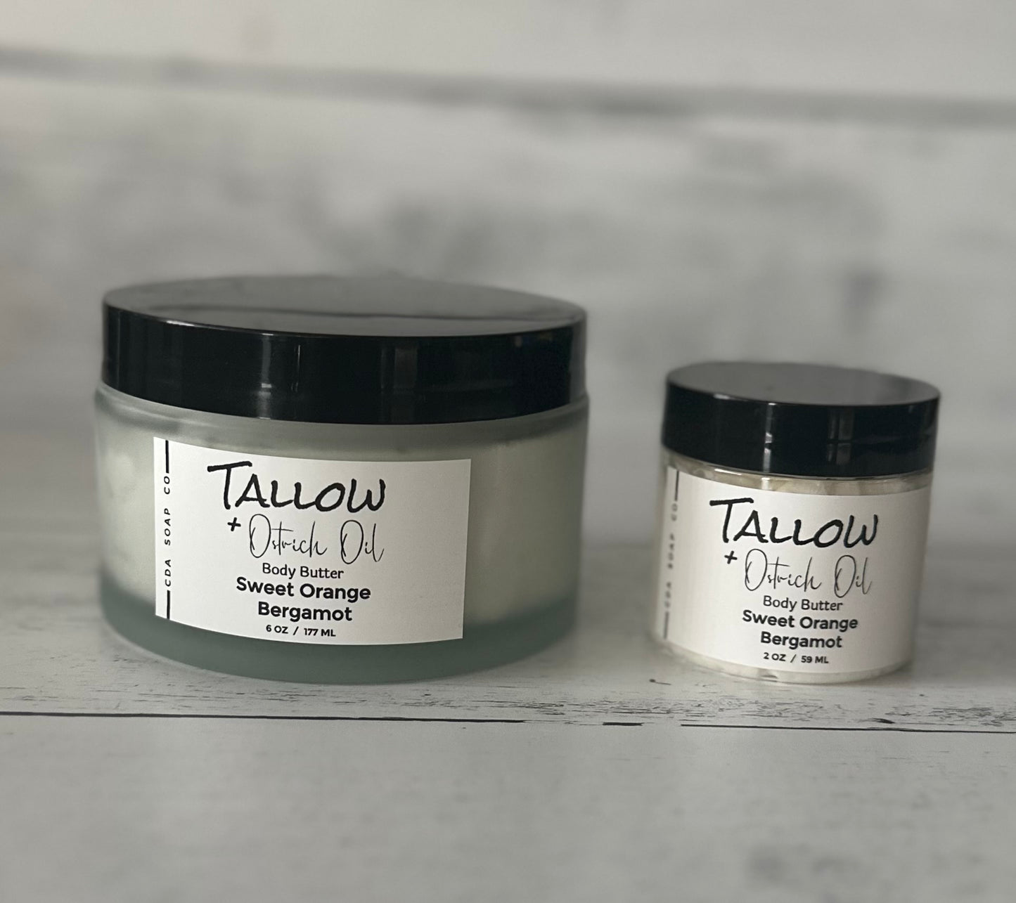 Two jars of Tallow + Oatrich Oil body butter on a gray surface with a neutral background.
