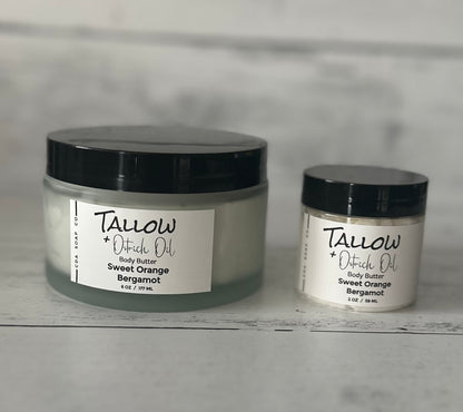 Two jars of Tallow + Oatrich Oil body butter on a gray surface with a neutral background.