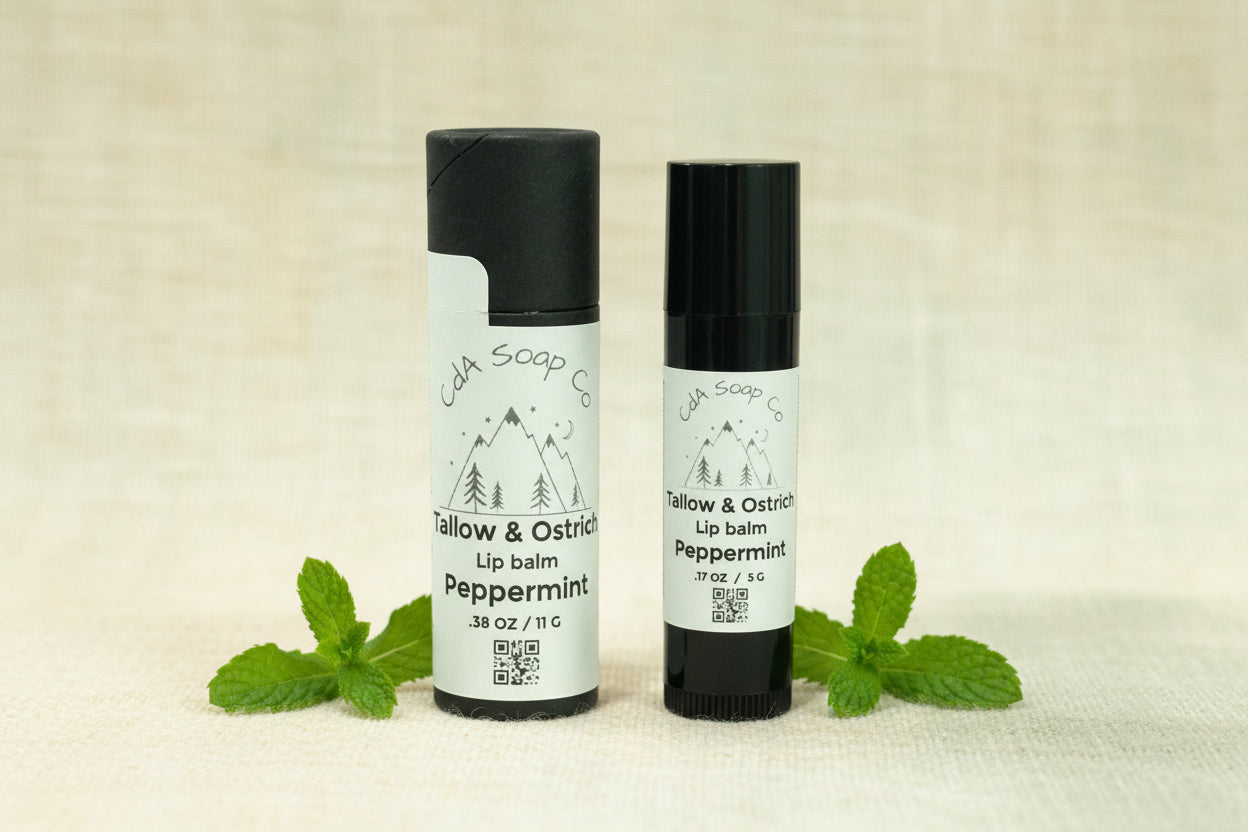 Two lip balm containers from CDA Soap Co on a off white background with peppermint accents 