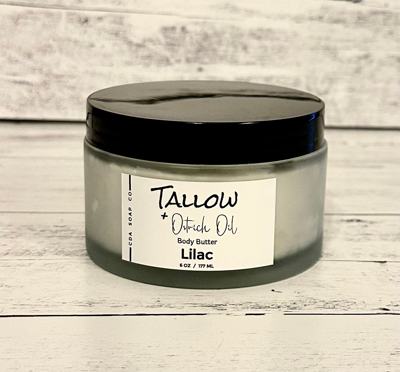 A frosted white glass jar with a black lid labeled 'Tallow Ostrich Oil Body Butter Lilac'.