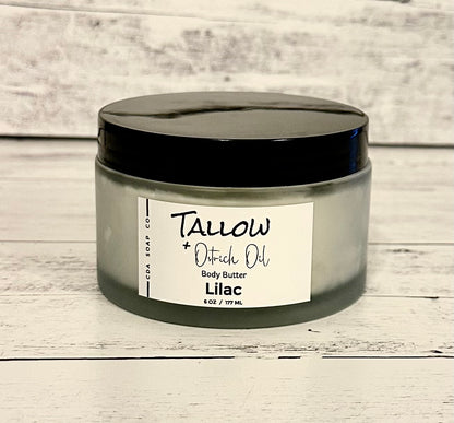 A frosted white glass jar with a black lid labeled 'Tallow Ostrich Oil Body Butter Lilac'.