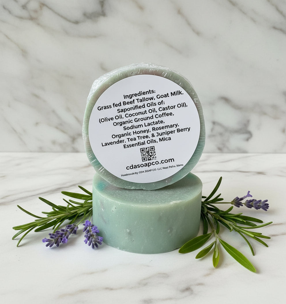Bar of soap with a label on a wooden surface with lavender and rosemary leaves.