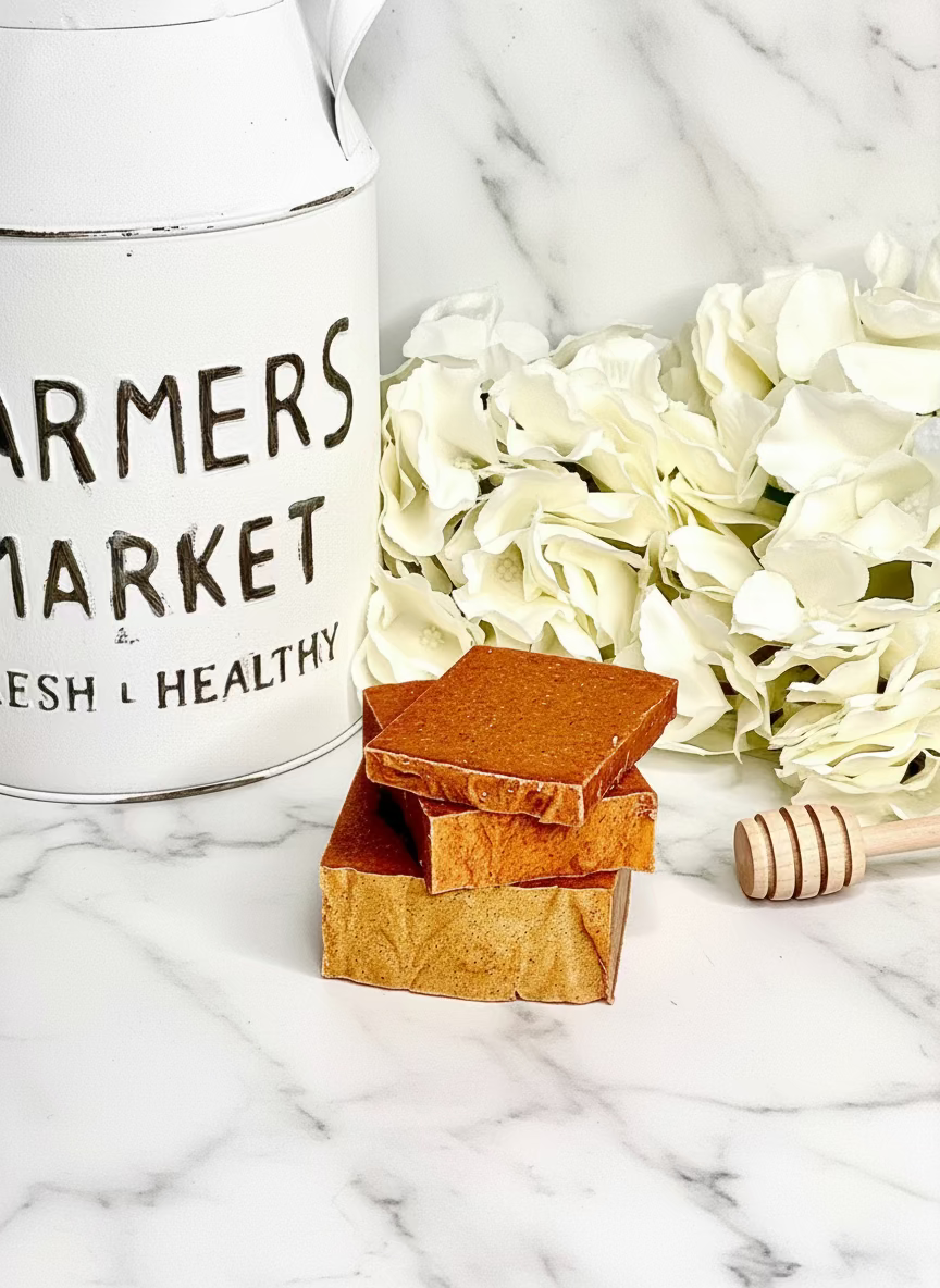 Stack of 3 dark orange soaps with a honey dipper and white flowers on a marble surface next to a 'Farmers Market' container.